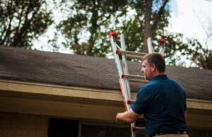 A man on a ladder inspecting a roof.